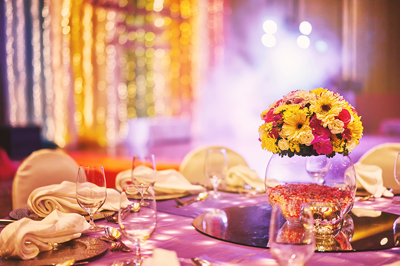 Wedding reception dinner table with flower bouquet decoration in the indian sangeet night with colorful lighting